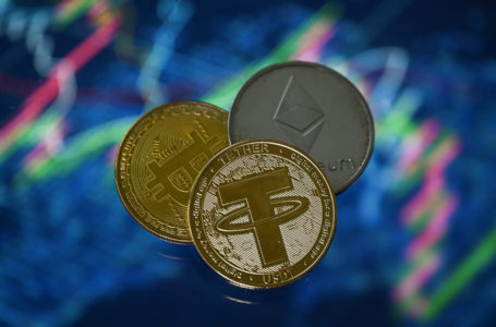 An illustration picture taken in London on May 8, 2022, shows gold plated souvenir cryptocurrency Tether (USDT), Bitcoin and Etherium coins arranged beside a screen displaying a trading chart. – Tether (USDT) is an Ethereum token known as a stablecoin that is pegged to the value of the US dollar, and is currently the largest stablecoin with a market value of USD 83 billion dollars. (Photo by Justin TALLIS / AFP)