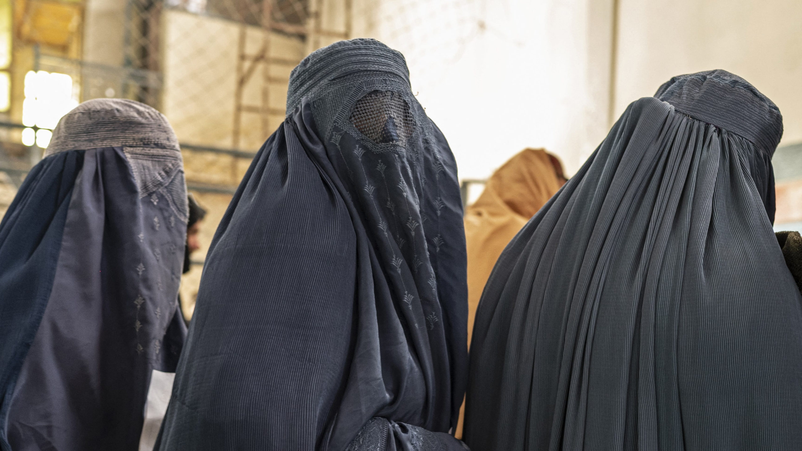Afghan burqa-clad women stand in a queue as they wait to receive food aid from a non-governmental organisation (NGO) at a gymnasium in Kabul on January 17, 2023. – At least three leading international aid agencies have partially resumed life-saving work in Afghanistan, after assurances from the Taliban authorities that Afghan women can continue to work in the health sector. (Photo by Wakil KOHSAR / AFP)